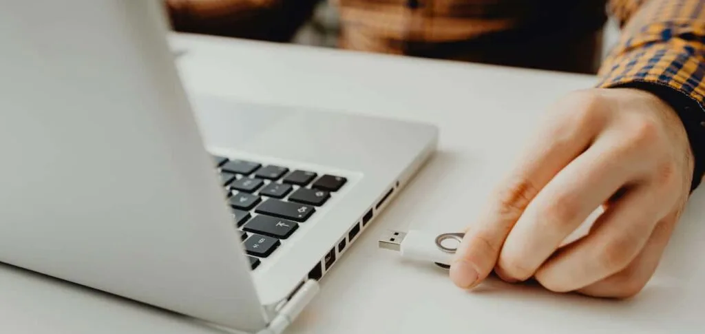 Main d'un entrepreneur branchant un périphérique USB sur son ordinateur portable pour illustrer la sécurité du matériel et des logiciels